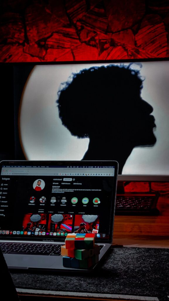Silhouette of person behind laptop with Rubik's cube on desk, modern studio setup.