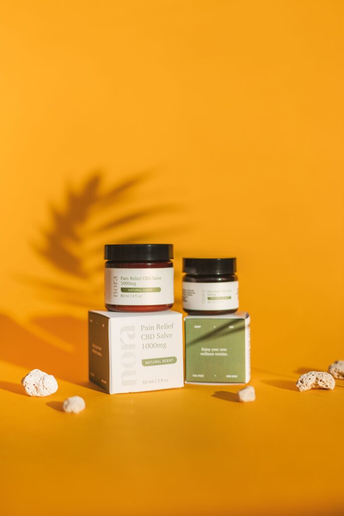 Product photography of CBD salve jars and boxes on an orange background with shadow effects.